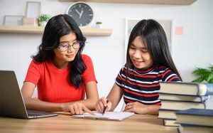 Two students studying together with books and a laptop