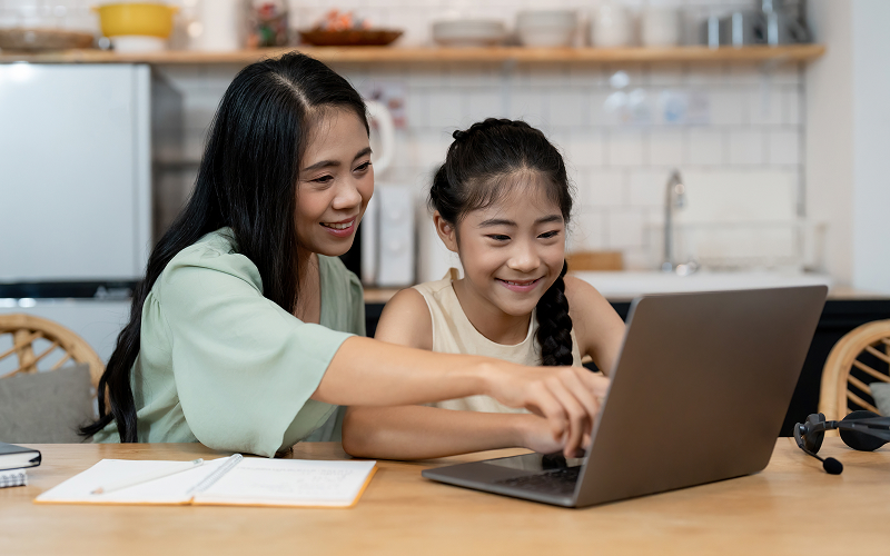Mother and daughter smiling while looking at a laptop together.