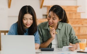 Two students studying together at a desk with a laptop and documents